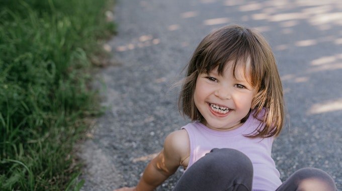 Ein kleines Mädchen sitzt auf dem Boden und lacht.