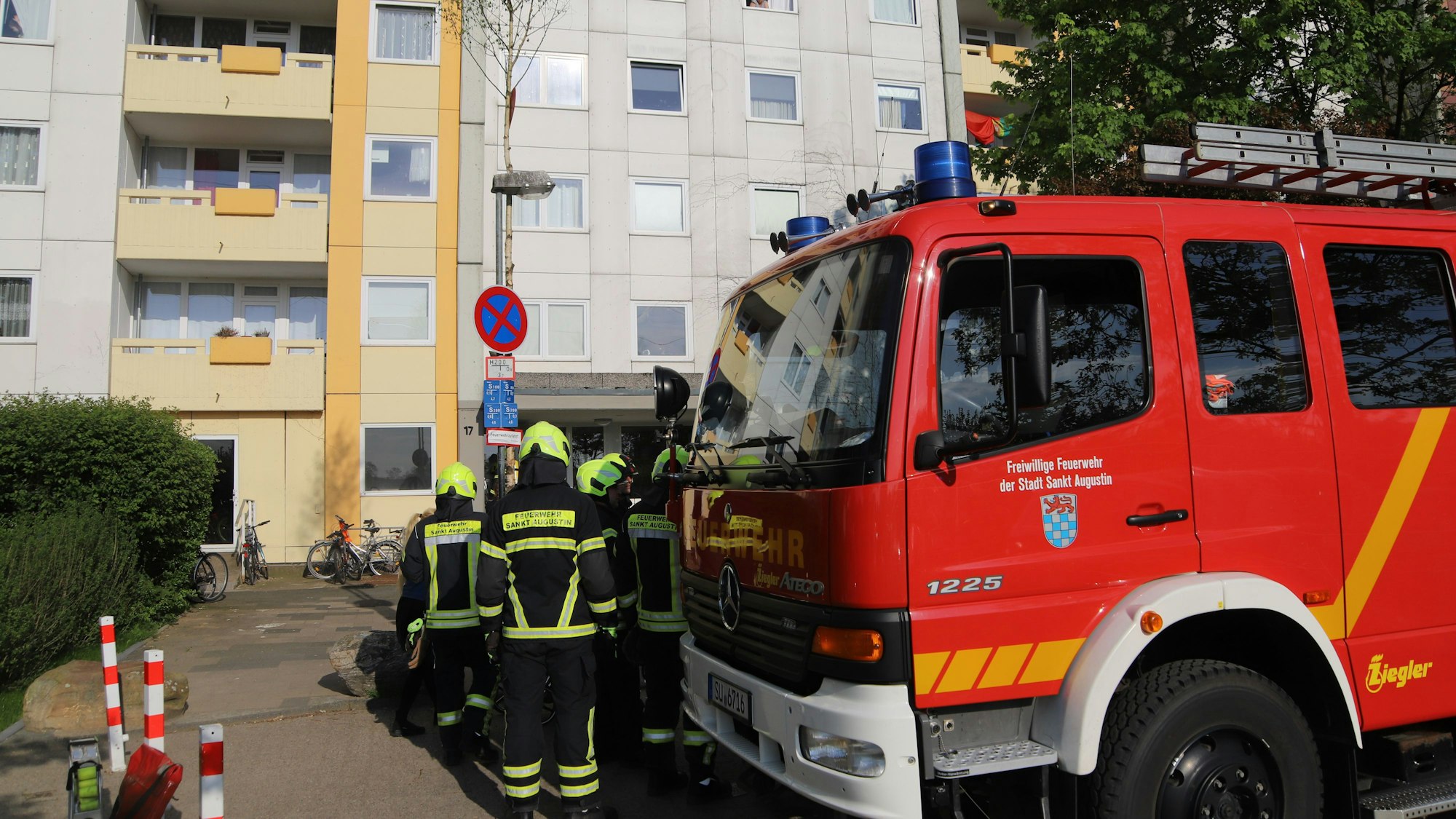 Einsatzkräfte der Feuerwehr stehen neben ihrem Fahrzeug vor einem Hochhaus.