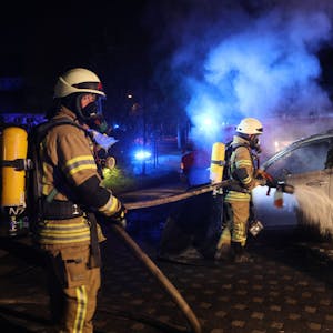 Zwei Feuerwehrmänner löschen ein qualmendes Auto.