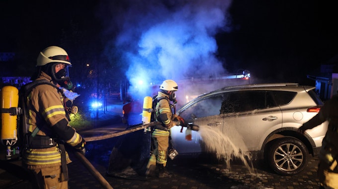 Zwei Feuerwehrmänner löschen ein qualmendes Auto.