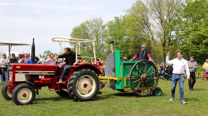Ein roter Traktor zieht eine Gulaschkanone vor Publikum über eine Wiese.