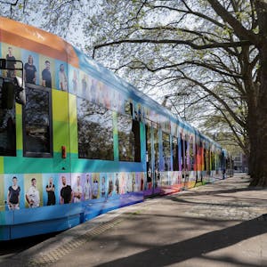 Stehende Straßenbahn, die mit bunten Kacheln und Fotos von KVB-Mitarbeitenden beklebt ist