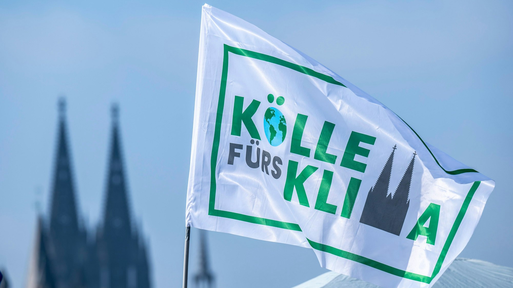 Ein Fahne mit der Aufschrift „Kölle fürs Klima“ weht vor dem Kölner Dom.