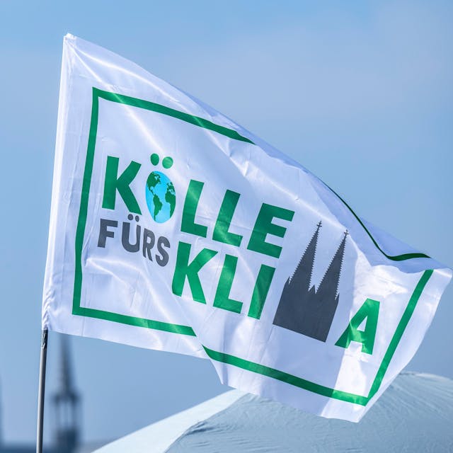 Weiße Fahne „Kölle fürs Klima“ vor dem Himmel, im Hintergrund die Domspitzen