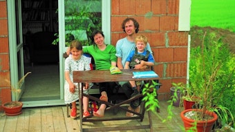 Eine Familie mit zwei Kindern sitzt lachend auf der Gartenterrasse.