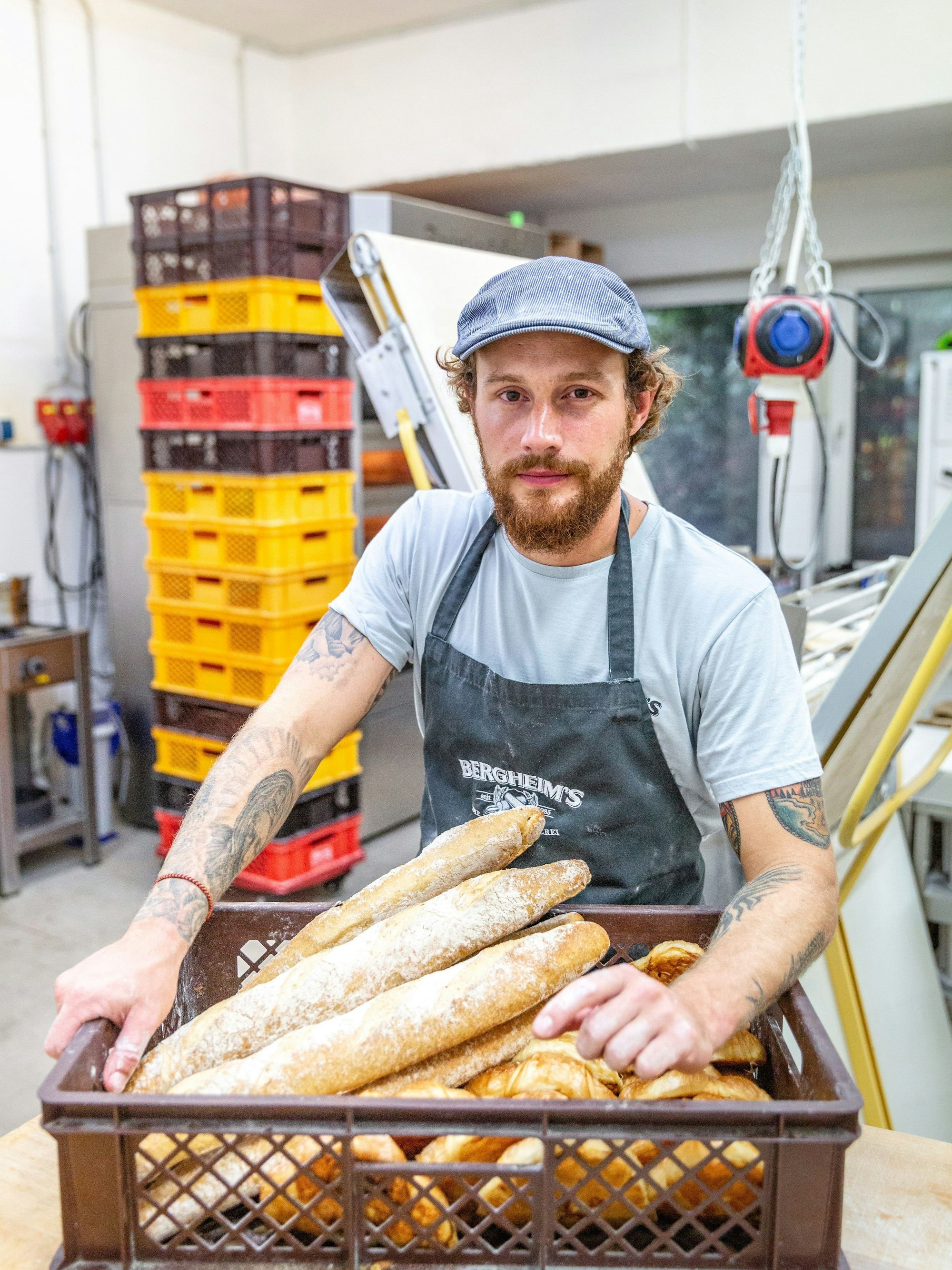 Bäckermeister Tim Bergheim  steht mit einem Korb voller Ciabatta-Brote in der Backstube der Bäckerei "Bergheim's - Die Meisterbäckerei".