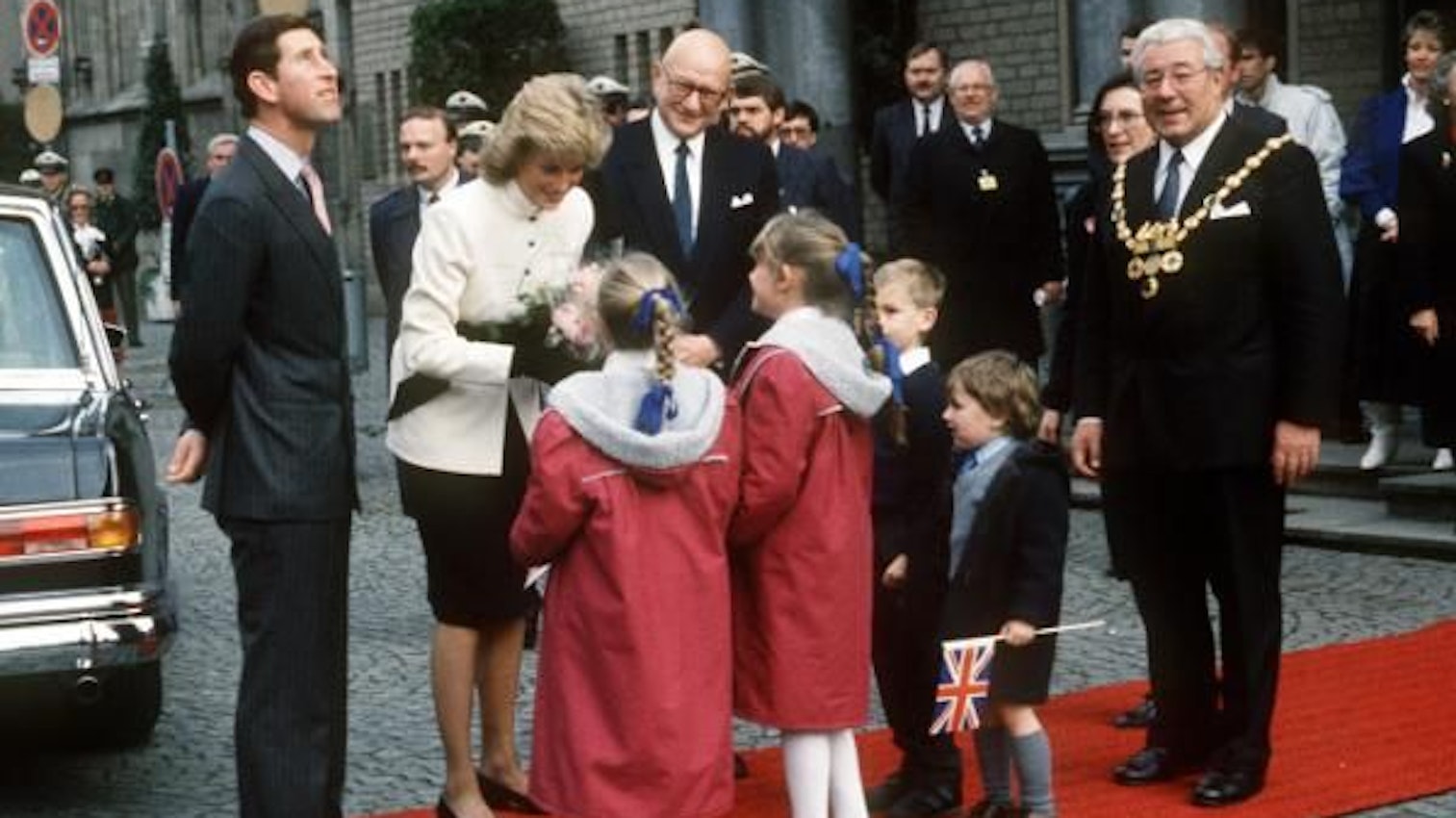 Der britische Kronprinz Charles (l) und seine Gattin Prinzessin Diana am 03.11.1987 in Köln. Während der Kronprinz sich umschaut und nach oben blickt, überreichen Kinder seiner Ehefrau Blumen. Rechts im Bild: Norbert Burger, damaliger Oberbürgermeister von Köln.
