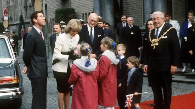 Der britische Kronprinz Charles (l) und seine Gattin Prinzessin Diana am 03.11.1987 in Köln. Während der Kronprinz sich umschaut und nach oben blickt, überreichen Kinder seiner Ehefrau Blumen. Rechts im Bild: Norbert Burger, damaliger Oberbürgermeister von Köln.
