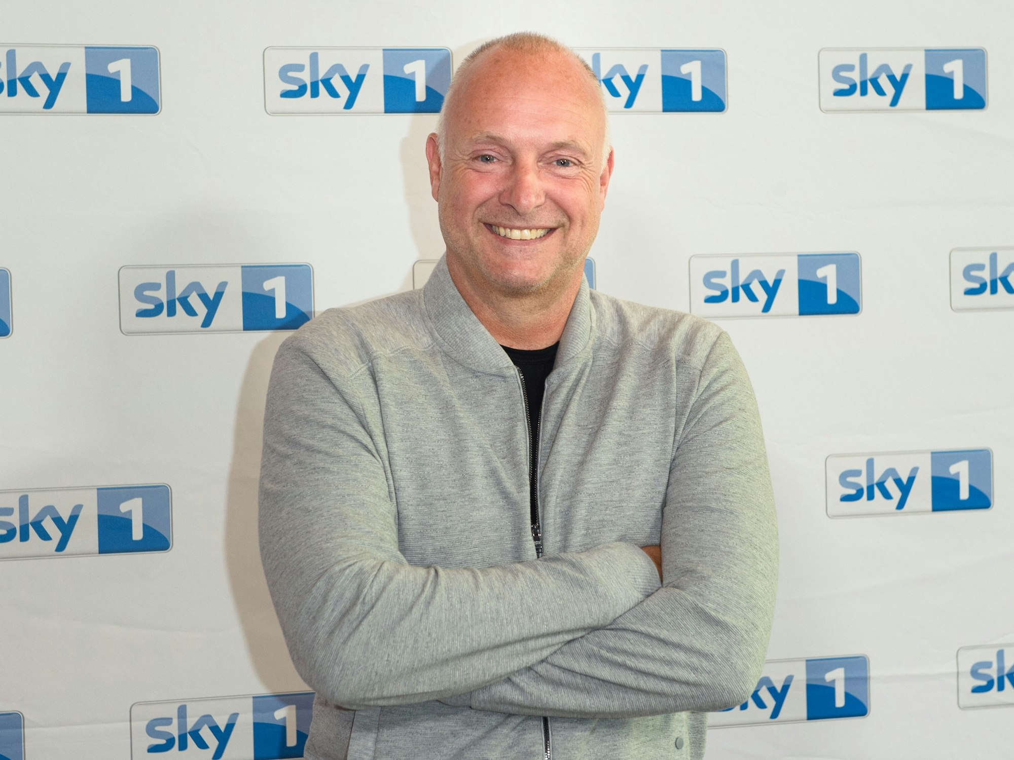 Frank Buschmann steht im Rahmen eines Pressetermins vor einer Logowand des Senders Sky.
