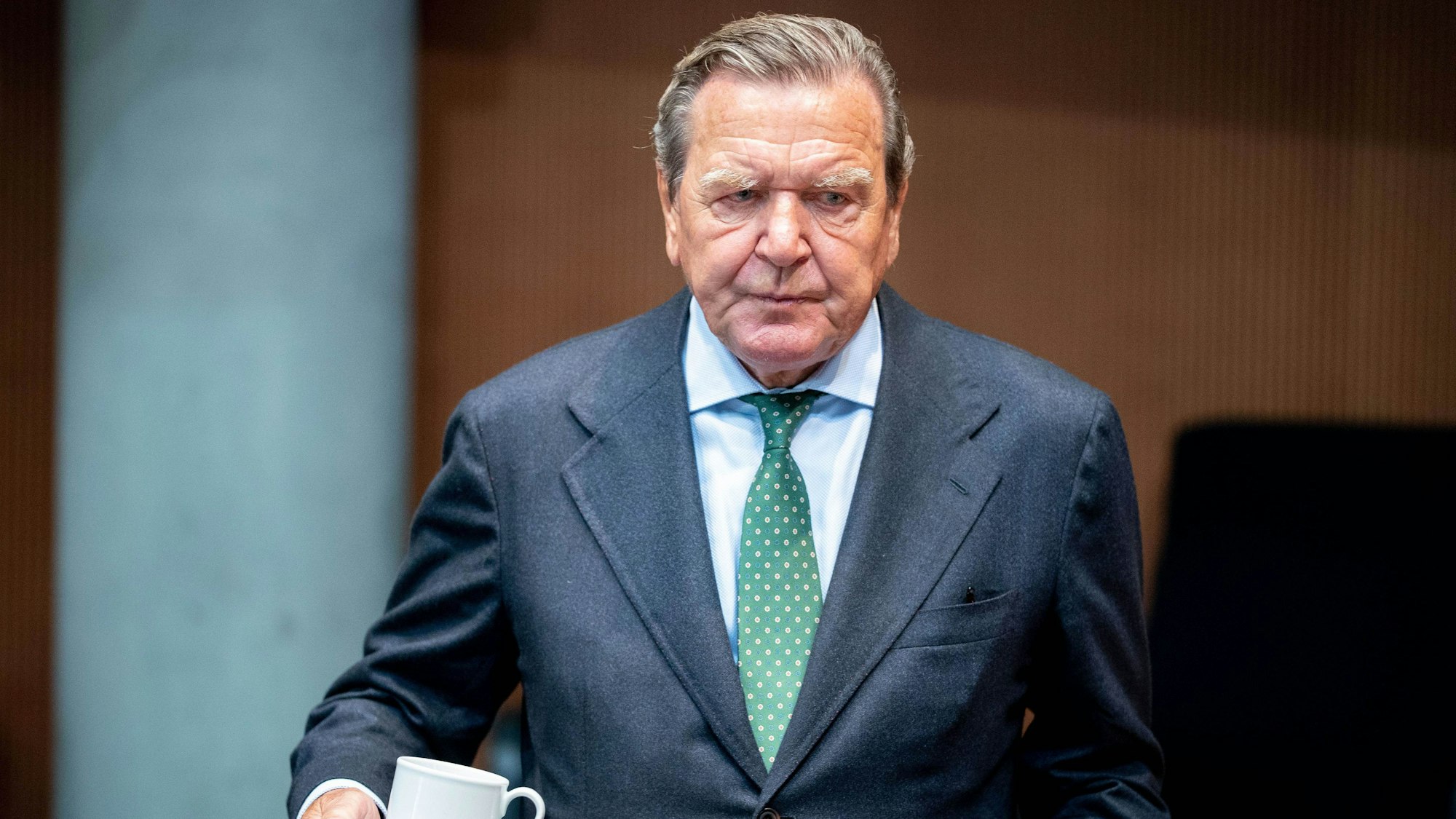 Altkanzler Gerhard Schröder (SPD) trägt eine Kaffeetasse durch einen Sitzungssaal im Deutschen Bundestag.