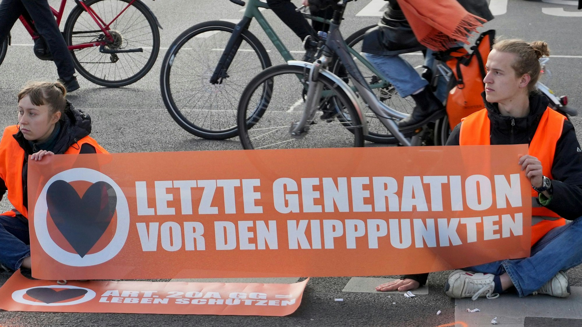Cyclists drive unhindered past climate activists who have their hands glued to the ground during a climate protest in Berlin, Germany, Thursday, April 27, 2023. Activists of the 'Letzte Generation' (Last Generation) blocked streets in Berlin on Thursday to protest against the climate policy of the German government. (AP Photo/Michael Sohn)