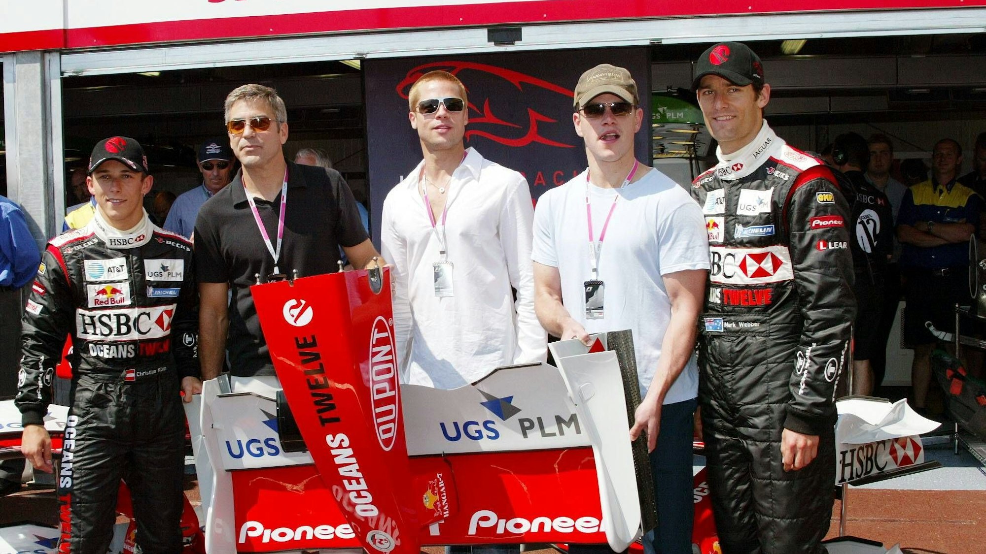 Die Schauspieler George Clooney (2.v.l.), Brad Pitt (Mitte) und Matt Damon (2.v.r.) anlässlich der „Oceans 12“-Filmpromotion zu Gast bei den Jaguar-Cosworth-Piloten Christian Klien (l.) und Mark Webber (r.)