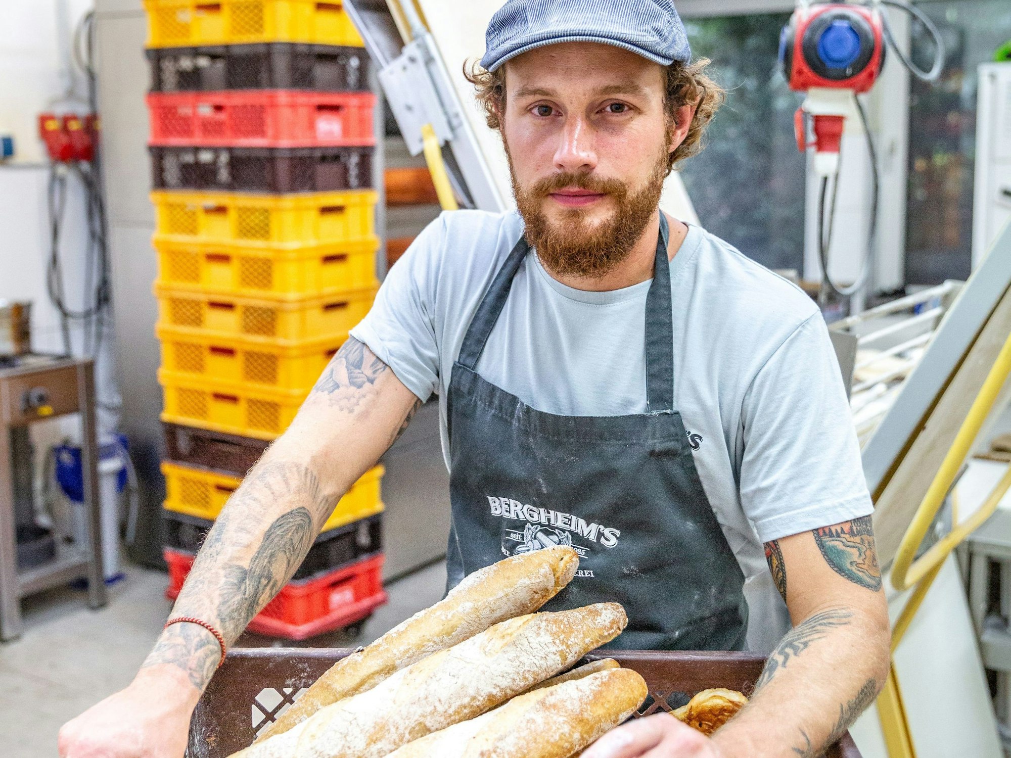Bäckermeister Tim Bergheim  steht mit einem Korb voller Ciabatta-Brote in der Backstube der Bäckerei „Bergheim's – Die Meisterbäckerei“.