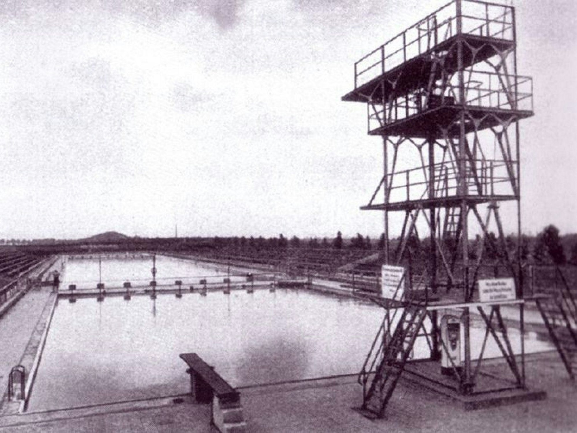 Eine Aufnahme aus den 20er Jahren: der etwas wackelig wirkender Sprungturm, dahinter die 100 Meter-Schwimmbahn.