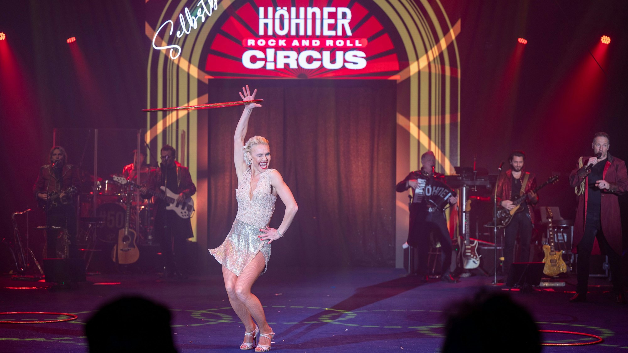 Eine Frau schwingt einen Reifen am Arm, im Hintergrund die Höhner und das Logo des Zirkus‘.
