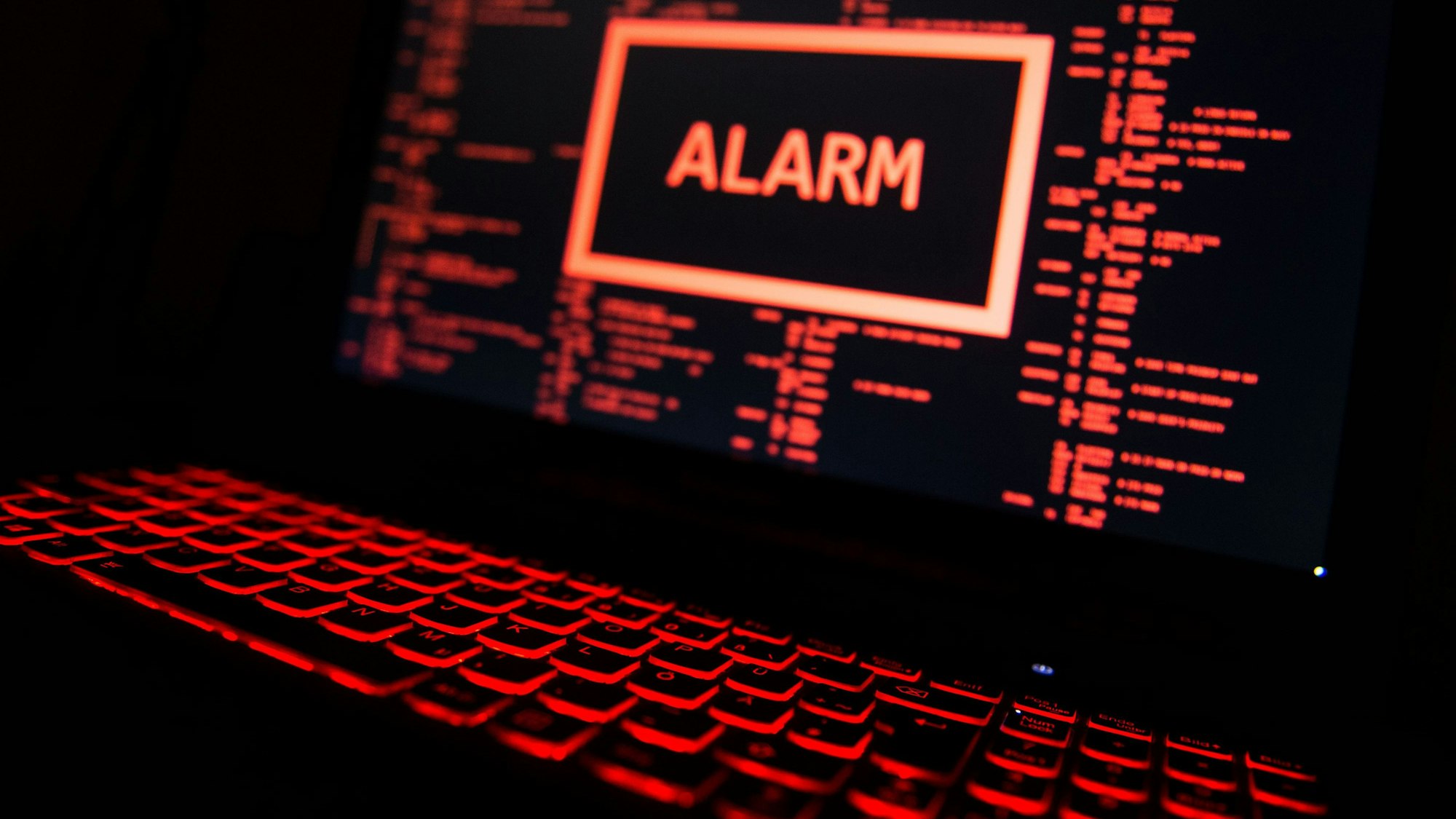Ein rot beleuchteter Computer zeigt eine fiktive Fehlermeldung an, in der Mitte des Bildschirms der Warnhinweis „Alarm“.
