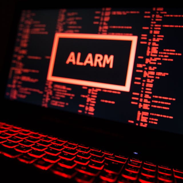 Ein rot beleuchteter Computer zeigt eine fiktive Fehlermeldung an, in der Mitte des Bildschirms der Warnhinweis „Alarm“.