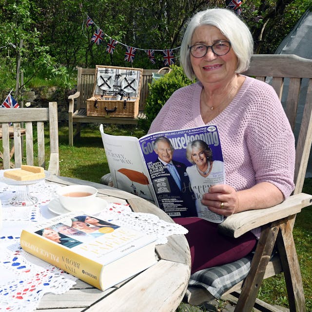 Eine Frau mit kinnlangen grauen Haaren sitzt in einem mit britischen Flaggen festlich geschmückten Garten.