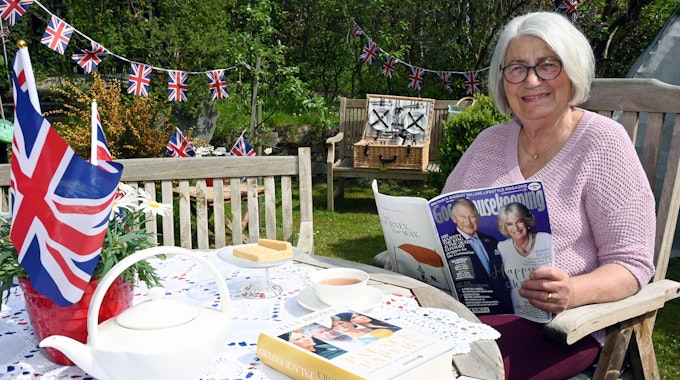 Eine Frau mit kinnlangen grauen Haaren sitzt in einem mit britischen Flaggen festlich geschmückten Garten.