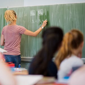 Das Bild zeigt eine Lehrerin vor ihrer Klasse an der Schultafel - Der Fachkräftemangel in Deutschland hat auch den Lehrberuf in hohem Maß erreicht.