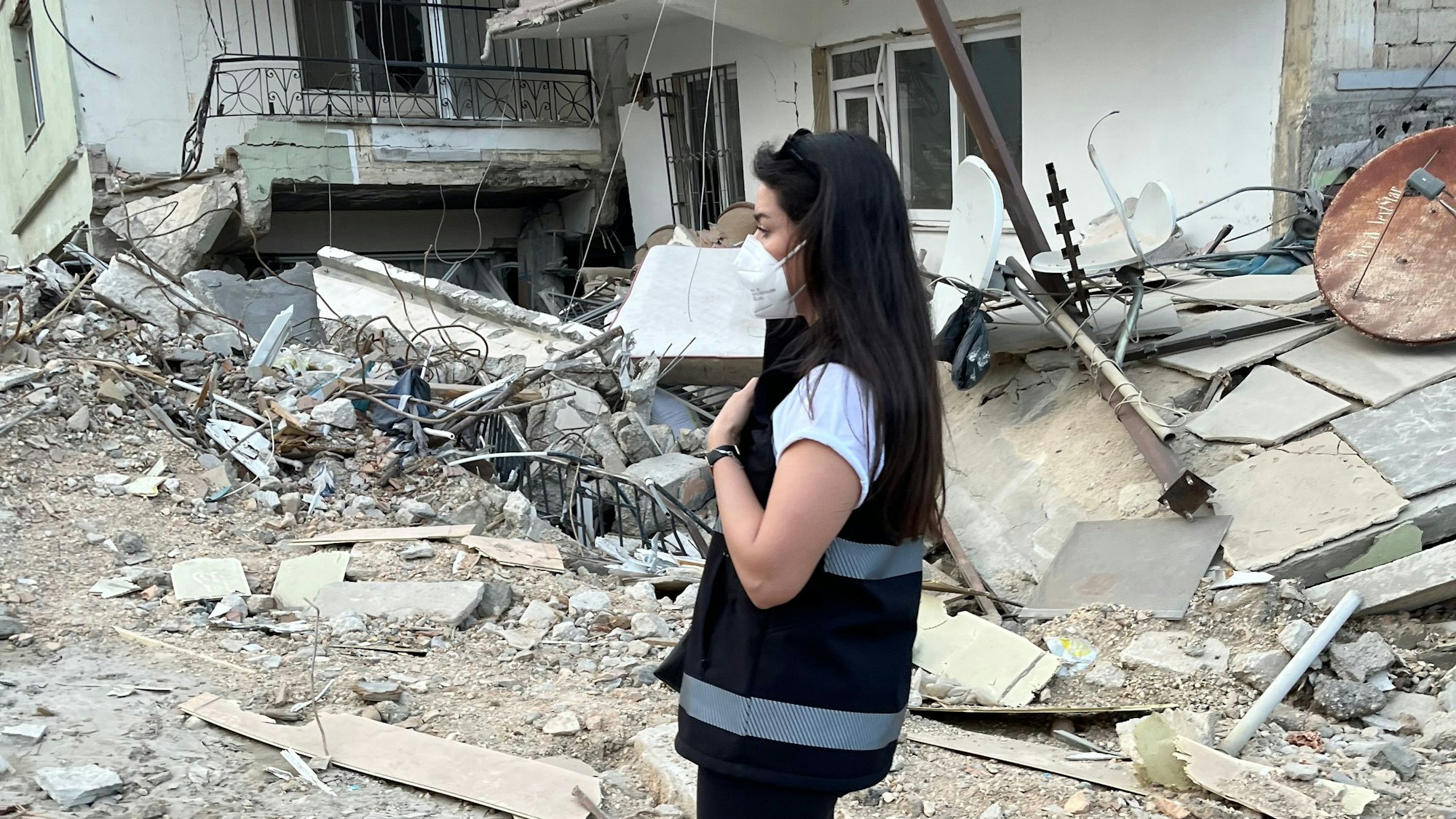 Lamia Faqirzada steht mit Maske in der zerstörten Stadt Antakya in Trümmern.