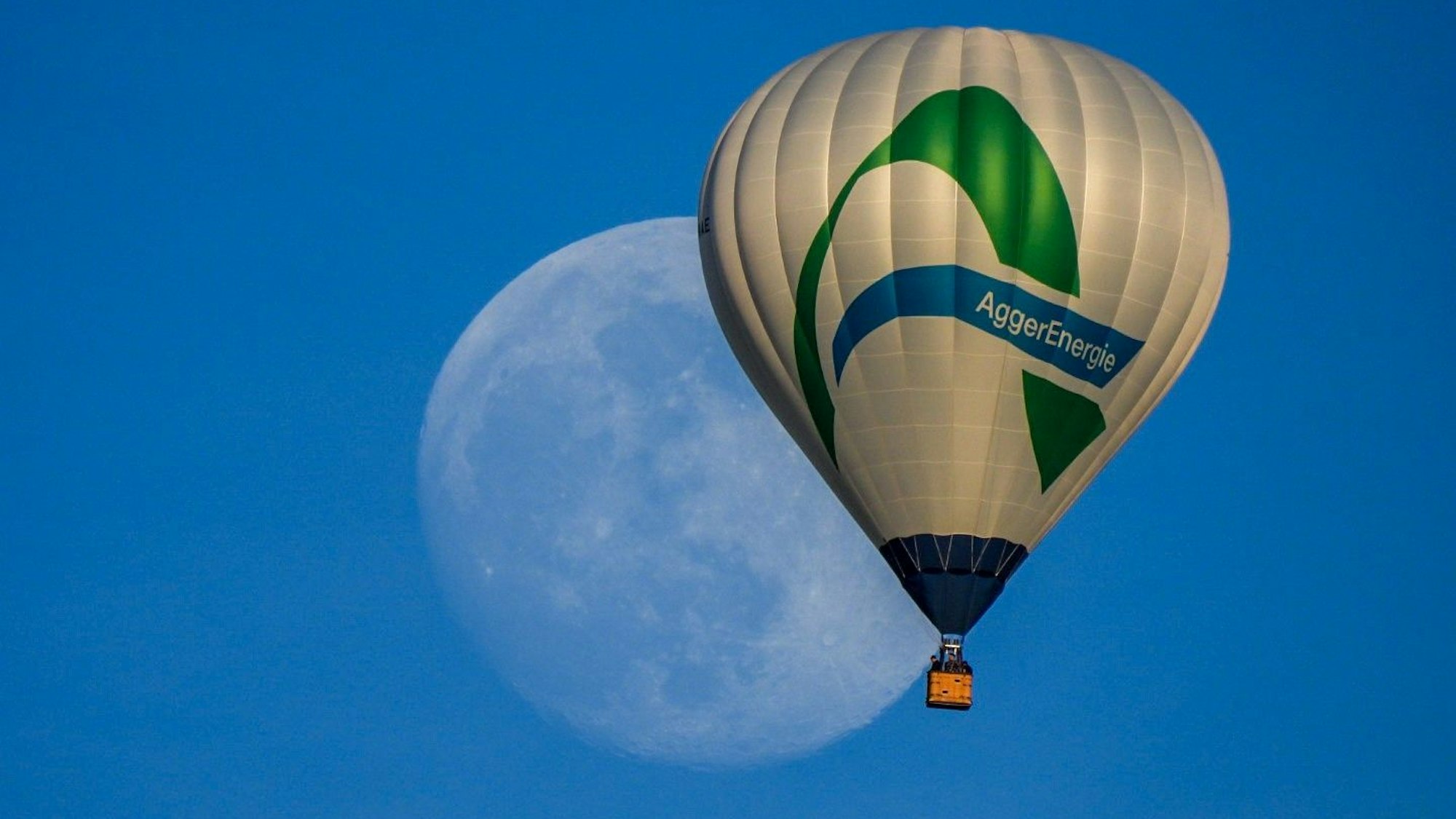 Ein Heißluftballon mit dem Logo der Aggerenergie fliegt am Himmel. Im Hintergrund des Ballons ist groß der Mond zu sehen.