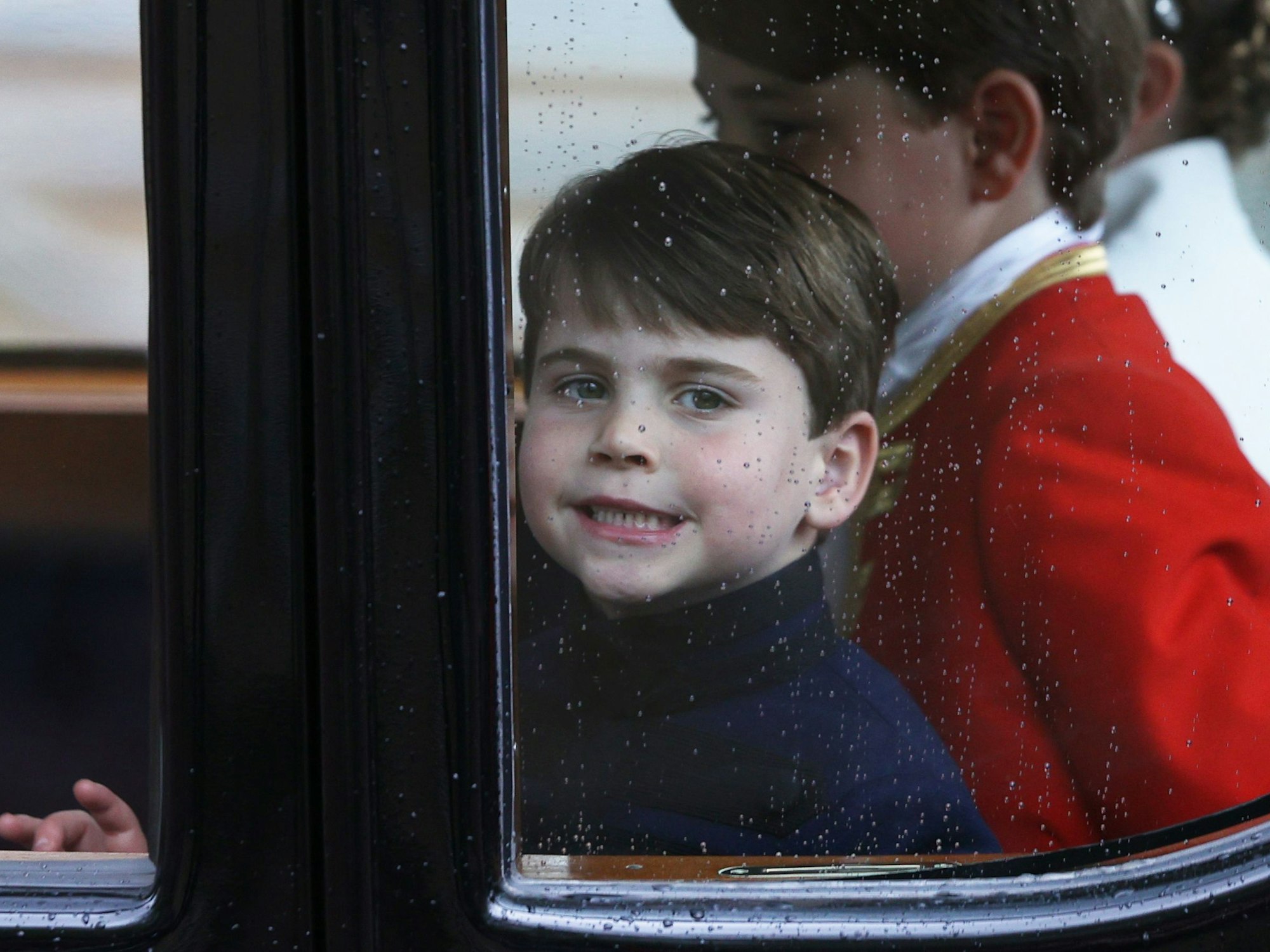 Prinz Louis von Wales lächelt aus dem Fenster, als er am 6. Mai 2023 in London mit seiner Familie von der Westminster Abbey zurück zum Buckingham Palace fährt.