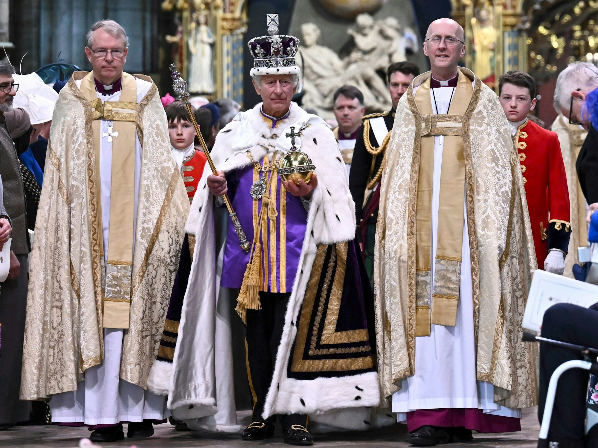 Großbritanniens König Charles III. (M) verlässt nach der Krönungszeremonie mit der Imperial State Crown, einem Zepter und dem Reichsapfel die Westminster Abbey.