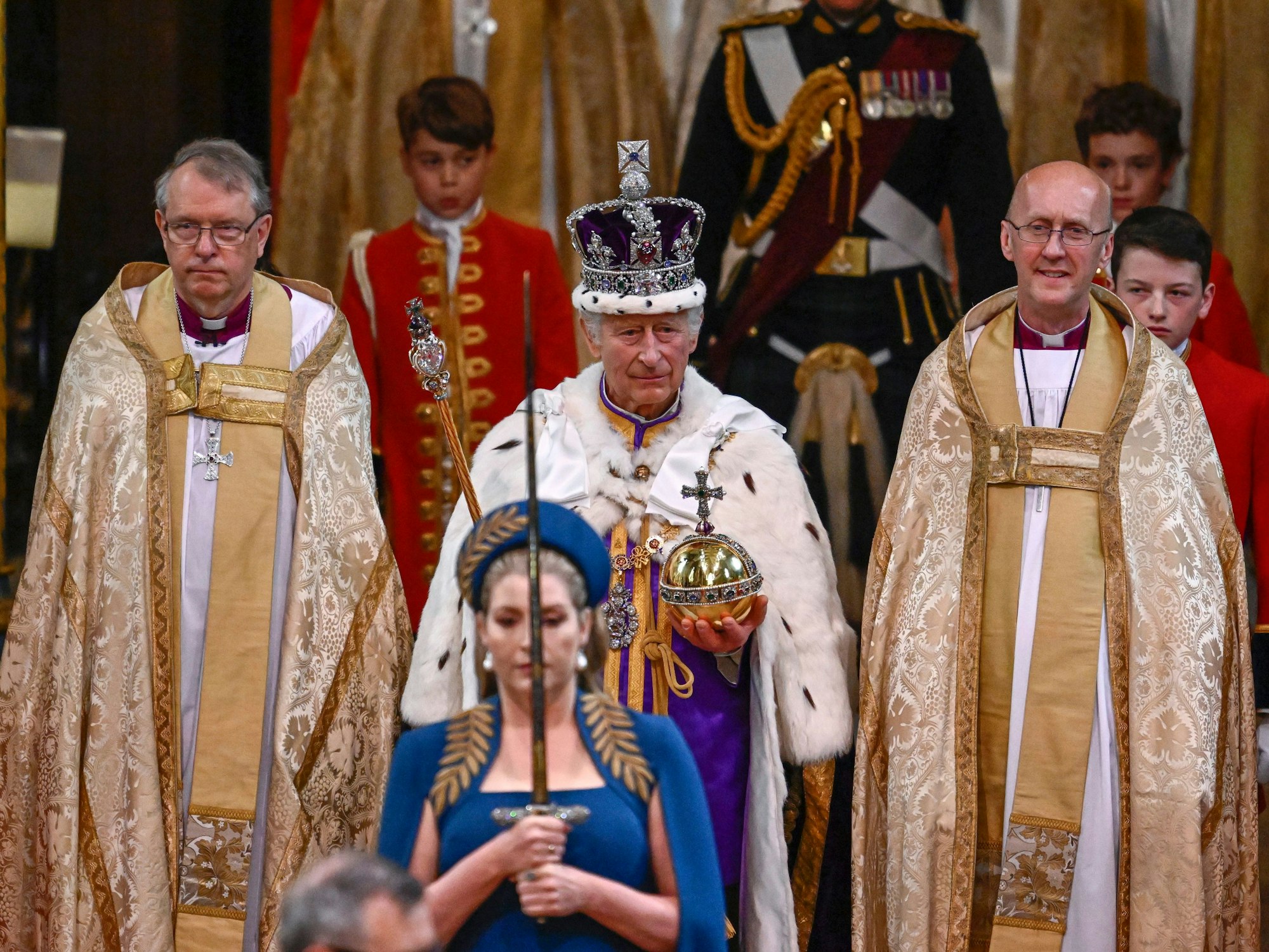 Großbritanniens König Charles III. (M) verlässt nach der Krönungszeremonie mit der Imperial State Crown, einem Zepter und dem Reichsapfel die Westminster Abbey.