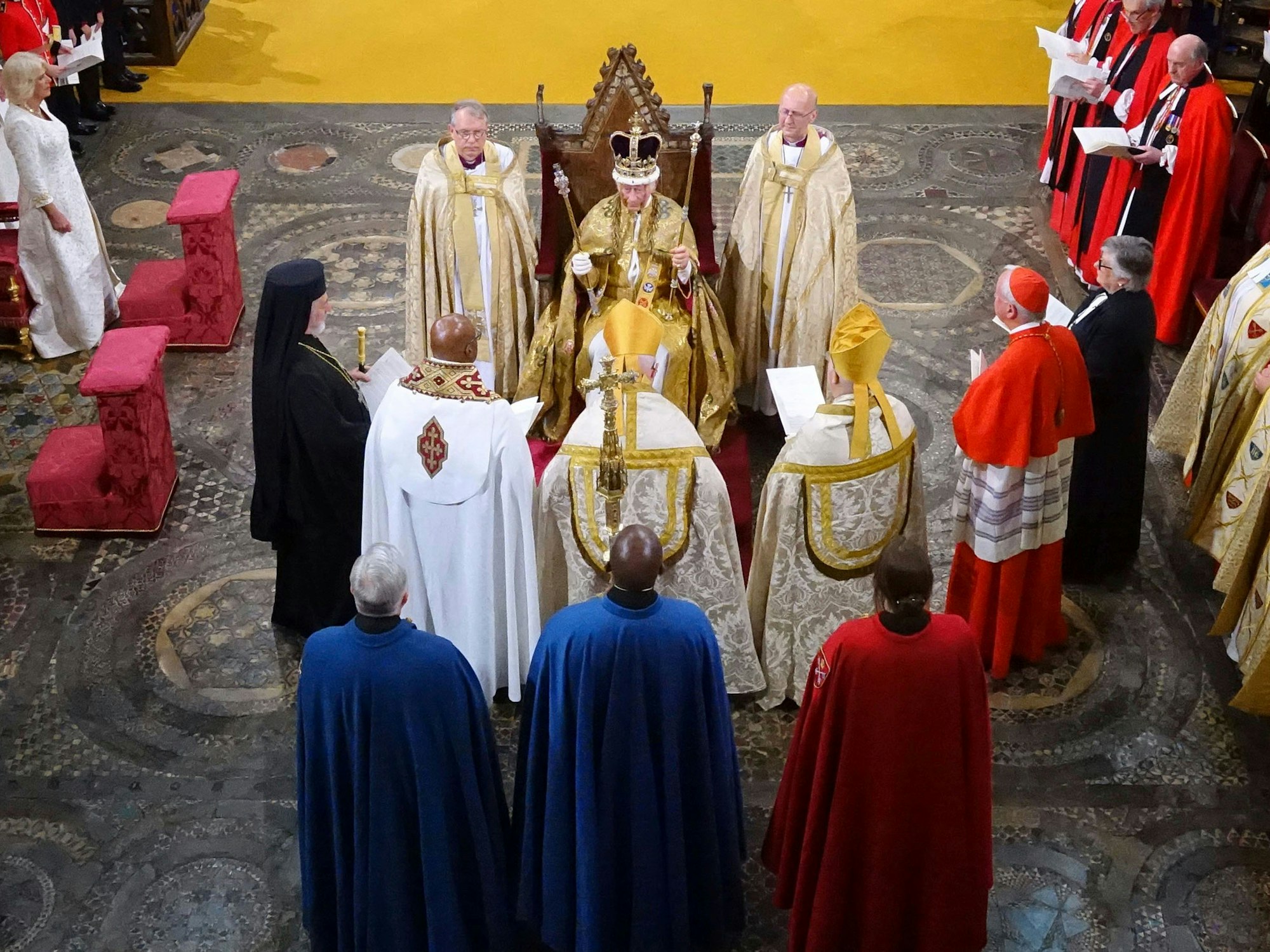 König Charles III. sitzt während der Krönungszeremonie nach der Krönung mit der Edwardskrone in der Westminster Abbey in einem Krönungsgewand auf dem Thron, in den Händen hält er zwei Zepter.