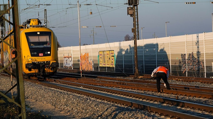 Ein Mitarbeiter der Bahn steht zwischen den Gleisen und greift nach einem Teil der Oberleitung.