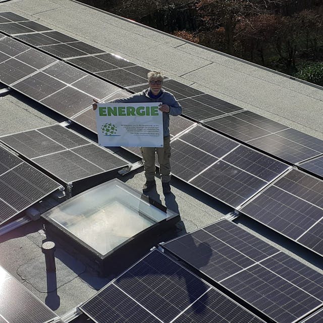 Stefan Häusler, Vorsitzender Klimafreunde Rhein-Berg, steht mit Plakat auf einem Dach mit Photovoltaikanlage.