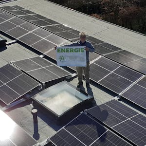 Stefan Häusler, Vorsitzender Klimafreunde Rhein-Berg, steht mit Plakat auf einem Dach mit Photovoltaikanlage.