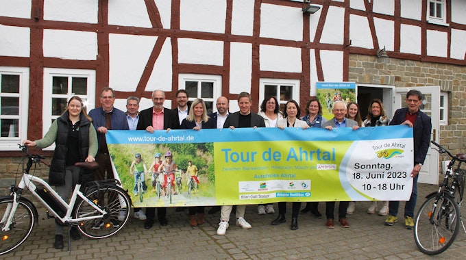 Die Vertreter der beteiligten Kreise und Kommunen halten vor einem Fachwerkgebäude in Antweiler ein Banner, mit dem für die „Tour de Ahrtal“&nbsp;geworben wird.