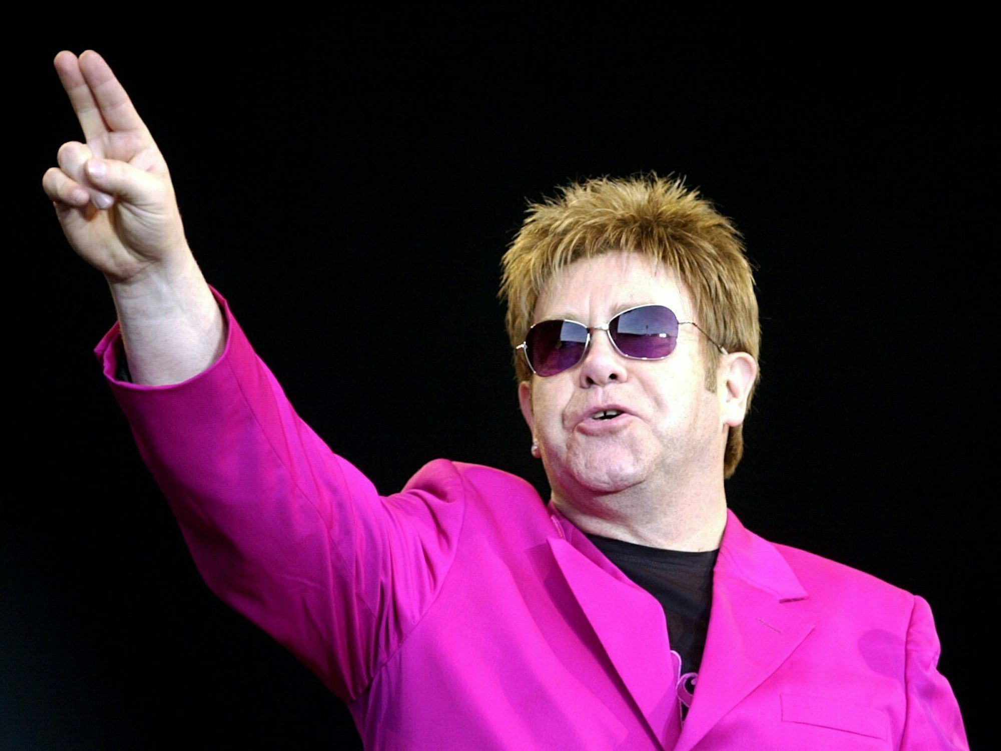 Popstar Elton John winkt im pinken Jackett seinen Fans