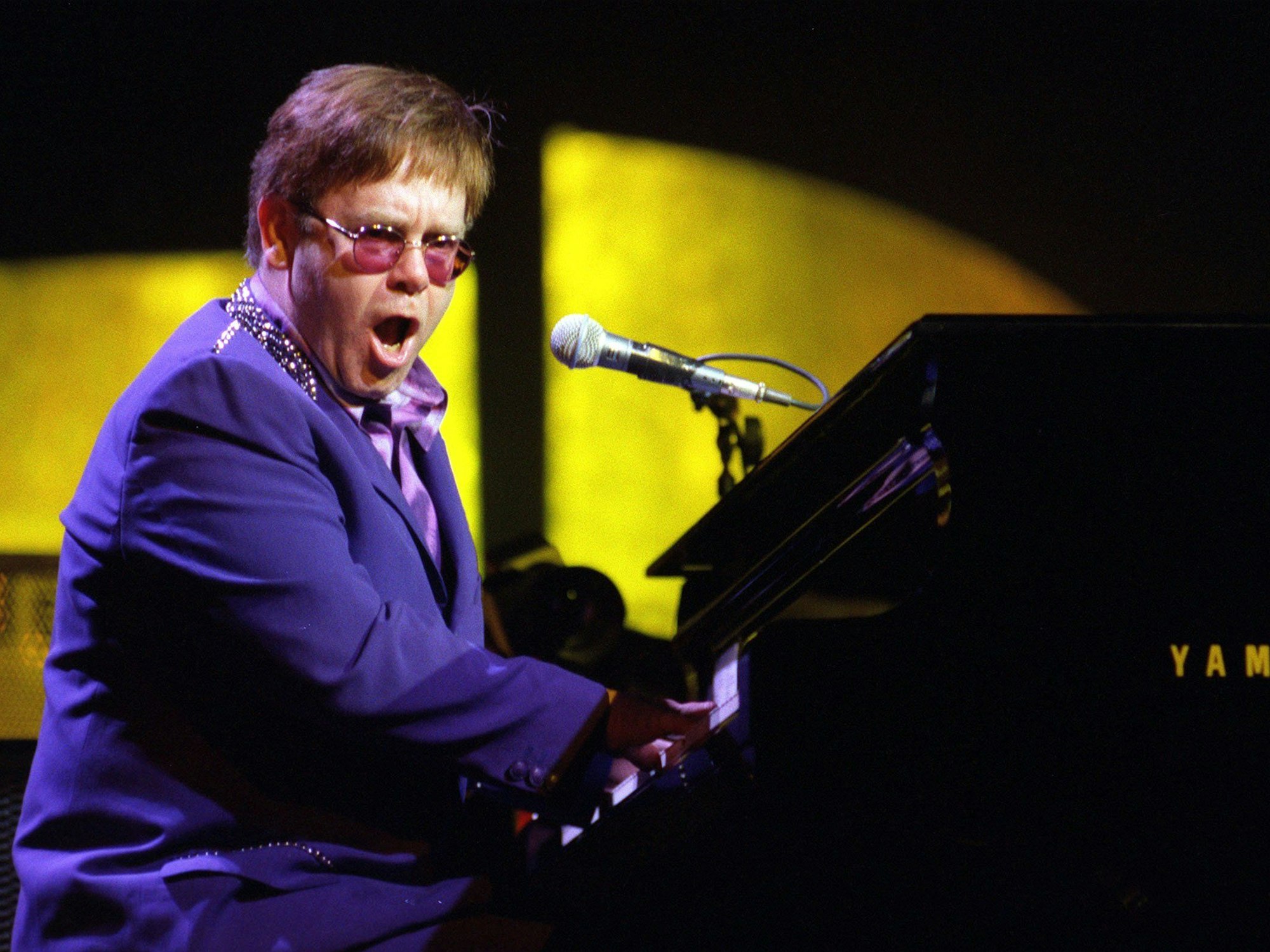 Elton John sitzt singend am Klavier
