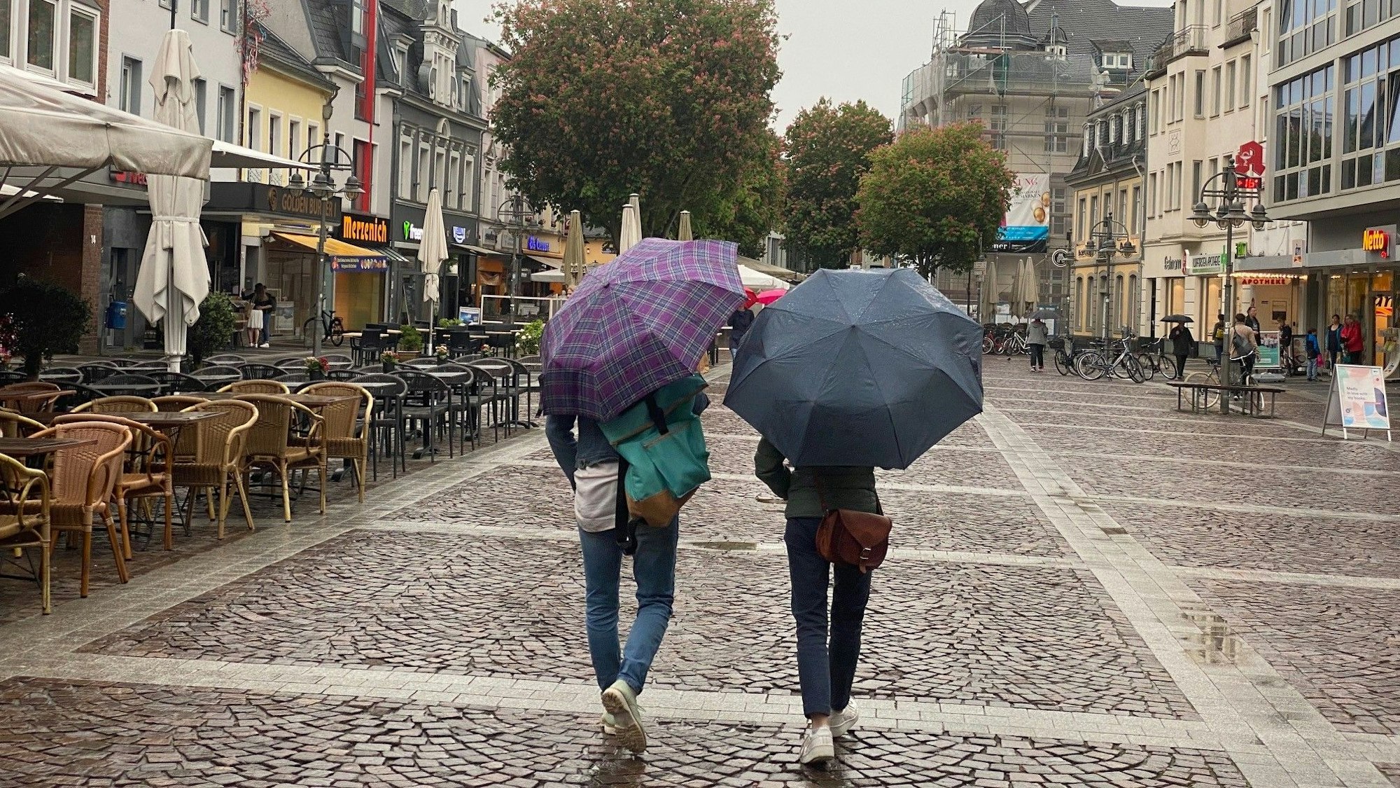 Das Foto zeigt die Fußgängerzone in Brüh. Zwei Personen gehen über die Uhlstraße, sie tragen Schirme, weil es regnet.