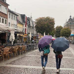Das Foto zeigt die Fußgängerzone in Brüh. Zwei Personen gehen über die Uhlstraße, sie tragen Schirme, weil es regnet.