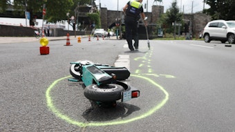 Auf der Rheinuferstraße in Köln liegt ein E-Scooter nach einem schweren Unfall auf der Straße. Ein Polizist markiert die Unfallstelle.