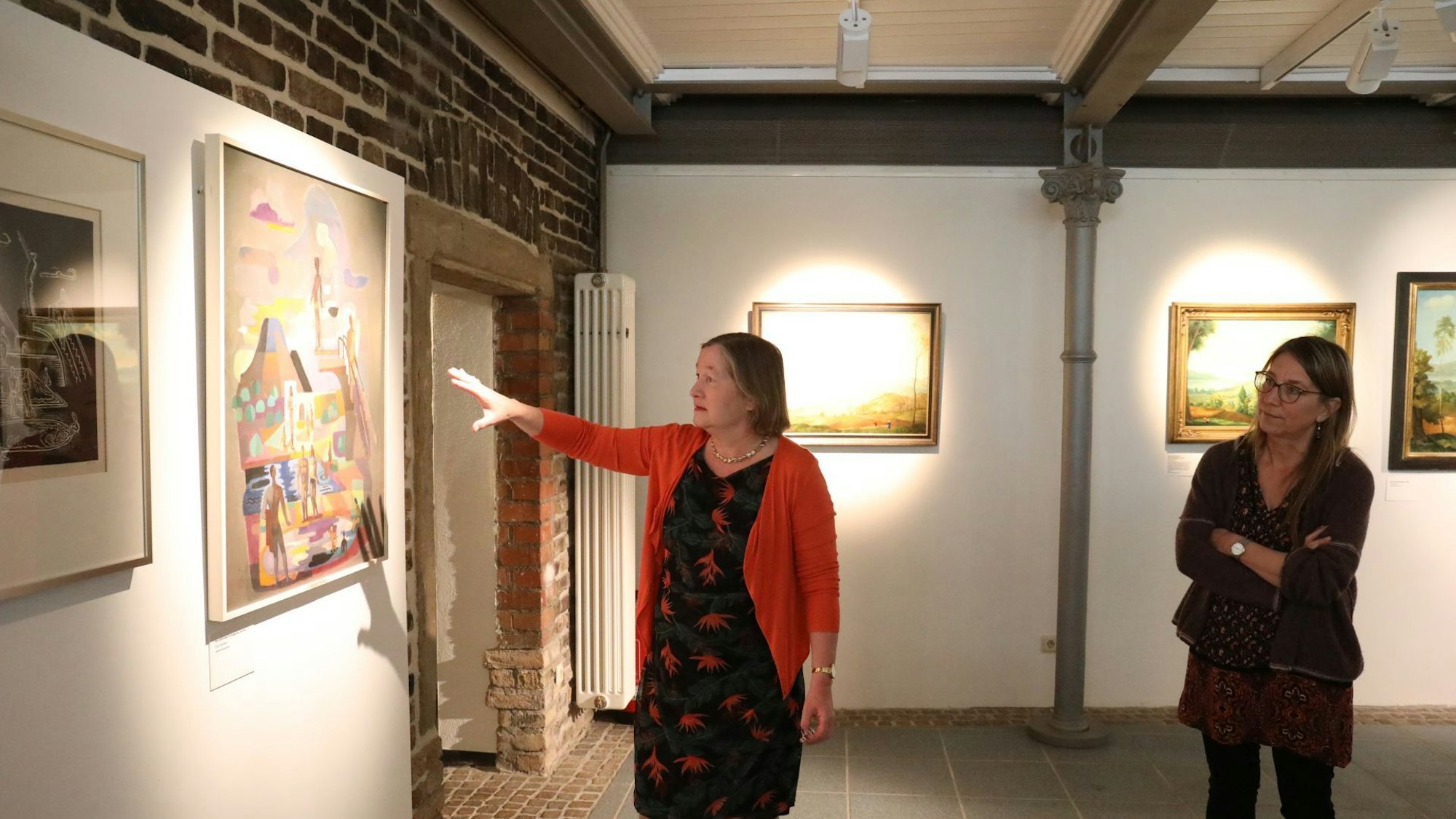 Zwei Frauen begutachten Gemälde in einer Ausstellung.