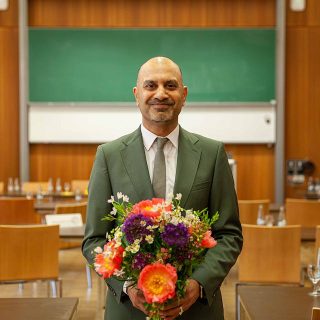 Professor Joybrato Mukherjee lacht in die Kamera und hält einen Blumenstrauß in den Händen.