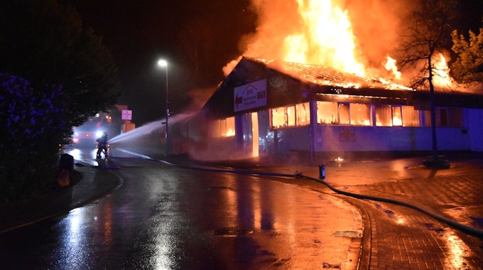 Eine Markthalle steht in Flammen. Ein Feuerwehrmann löscht.