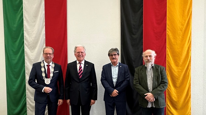 Das Foto zeigt Bürgermeister Volker Mießeler und die neuen Bergheimer Ehrenbürger Johannes Hübner, Helmut Paul und Peter Hirseler. Sie stehen vor den Flaggen von NRW und Deutschland.