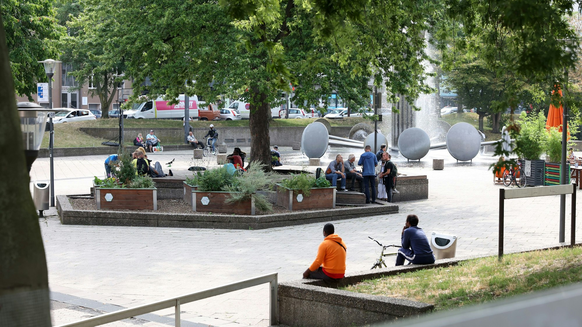 Mehrere Menschen sitzen auf Mauern rund um den Brunnen auf dem Kölner Ebertplatz.