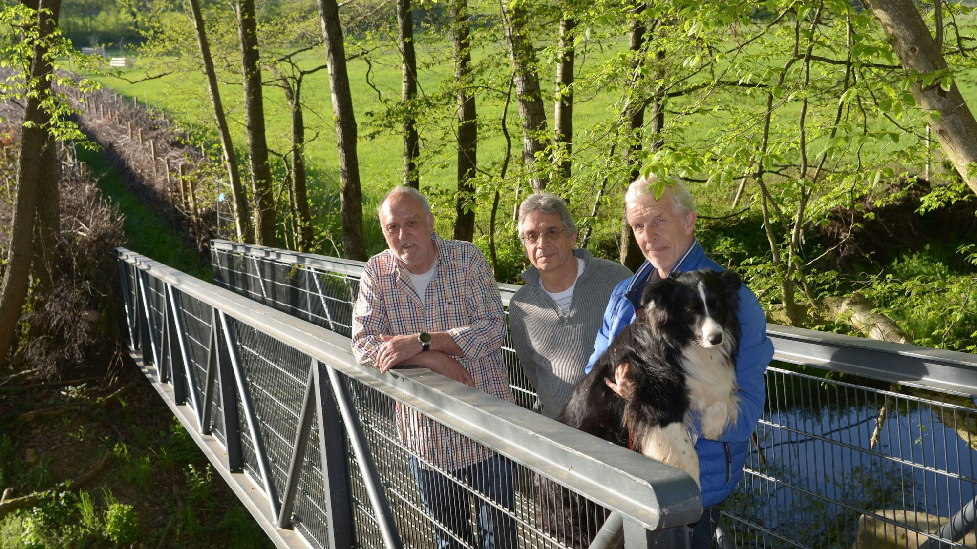 Die drei Männer stehen auf der Brücke und blicken in die Kamera. Wilfried Steinkrüger hält einen Hund auf dem Arm.