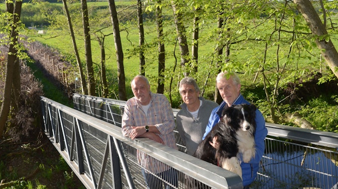 Die drei Männer stehen auf der Brücke und blicken in die Kamera. Wilfried Steinkrüger hält einen Hund auf dem Arm.