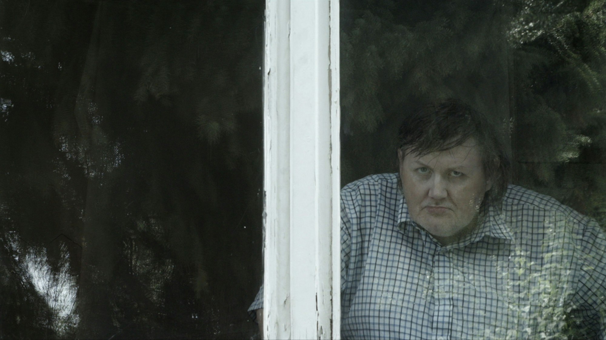 Ein grimmig dreinblickender Mann schaut zum Fenster seiner Wohnung heraus.