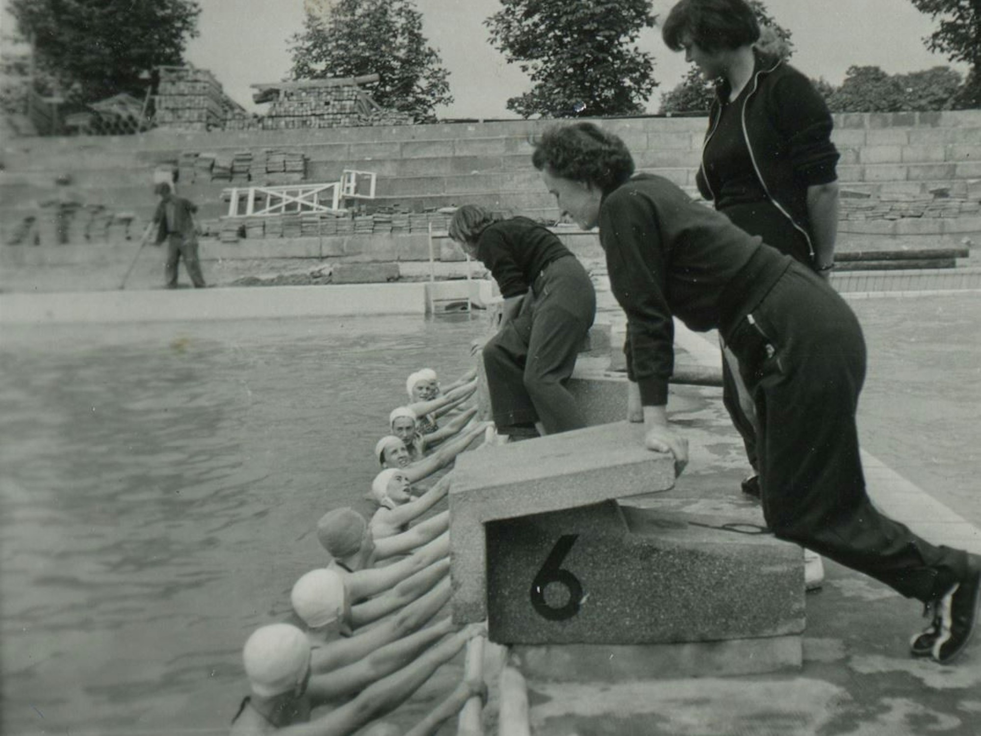 Studenten und Studentinnen 1954 bei einer Lehrveranstaltung im Stadionbad. Im Hintergrund wird die Tribüne ausgebessert.
