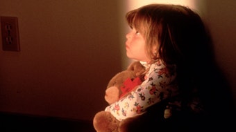 Ein kleines Mädchen hält einen Teddybären in der Hand und schaut beängstigt nach oben