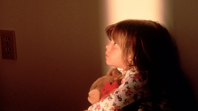 Ein kleines Mädchen hält einen Teddybären in der Hand und schaut beängstigt nach oben